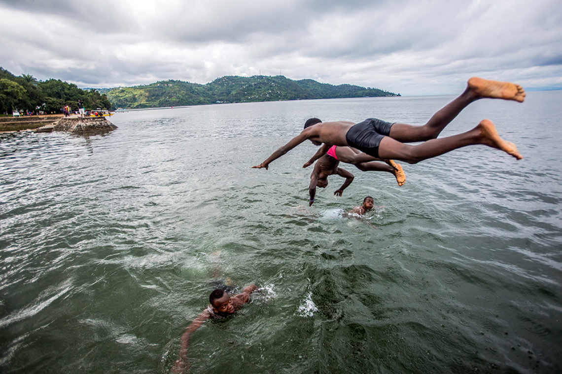 Two boys dive into a lake as two other boys swim.