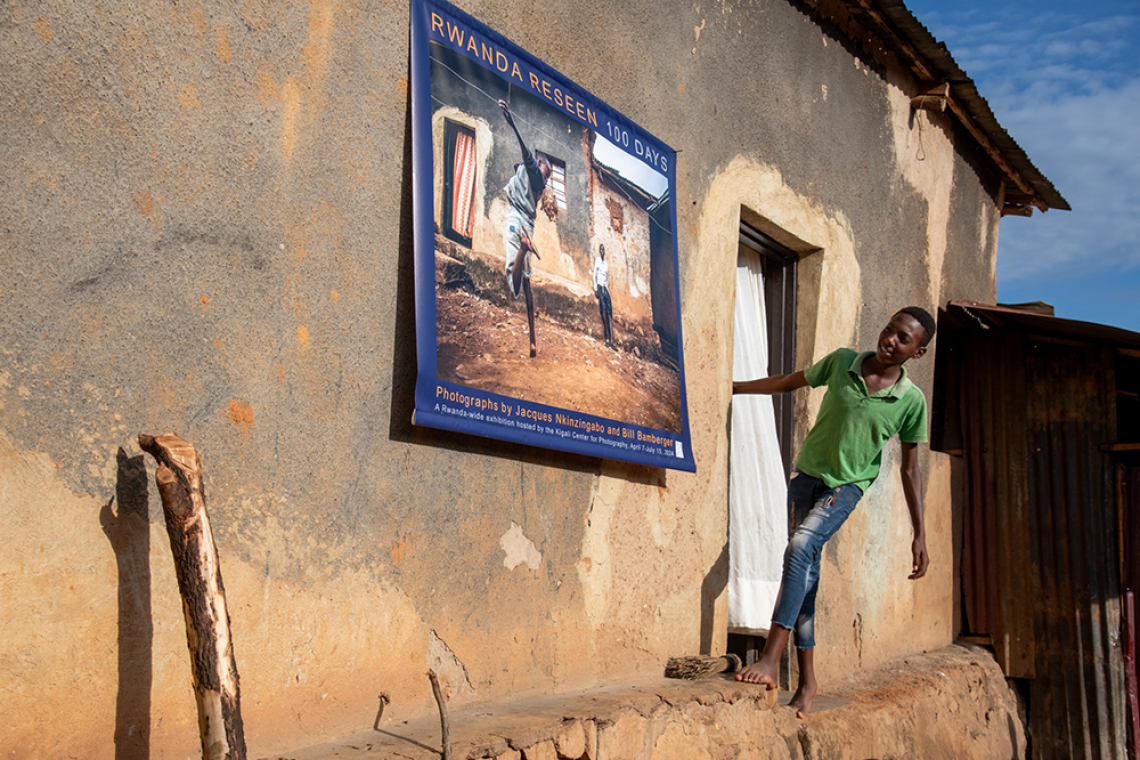 A boy looks at a large printed photograph from the Rwanda Reseen exhibition in which he is playing soccer.