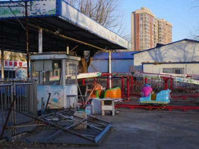 A dilapidated playground with faded colors with a brown and white high-rise building behind it