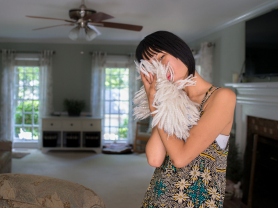 Mia with fur, 2016 by Mary Berridge; a young woman holds a fuzzy accessory up to her face while standing in a living room.
