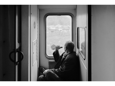 A man sits inside a train near the doorway and looks out the window.