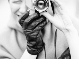 Black and white photo of person holding a camera to their eye and adjusting the lens.