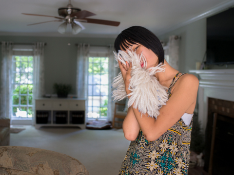 Mia with fur, 2016 by Mary Berridge; a young woman holds a fuzzy accessory up to her face while standing in a living room.