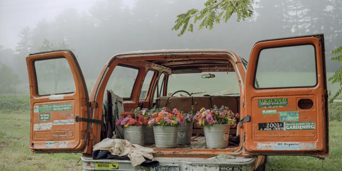 Rear view of an orange van with back doors open, showing cut flowers in silver buckets.